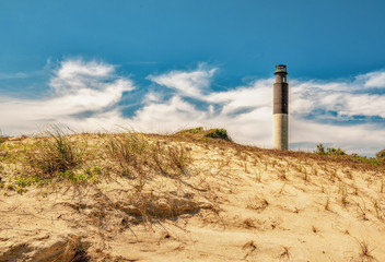 A beautiful lighthouse landscape over sand dunes and a cloudy blue sky in high definition.