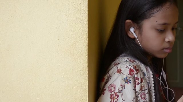 Long hair cute girl listening music from mobile phone with earphones in chino portuguese style building.