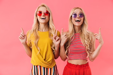Obraz premium Happy blonde twins in sunglasses pointing and looking up