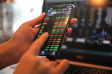 Female hand with smartphone trading stock online in coffee shop , Business concept