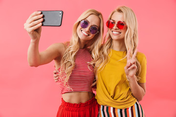 Happy blonde twins in sunglasses having rest and making selfie