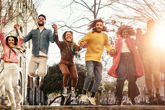 Group of happy friends jumping outdoor - Millennial young people having fun dancing and celebrating at sunset outside - Friendship, urban life and youth lifestyle concept