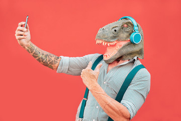 Crazy senior man wearing t-rex mask and taking selfie with mobile smartphone - Hipster older male...