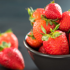 Delicious strawberries in a bowl on black background.