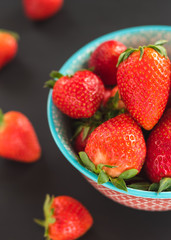 Delicious strawberries in a bowl on black background.