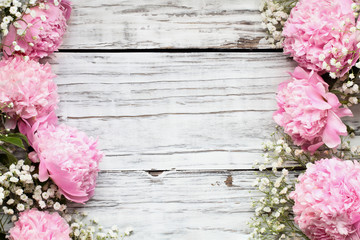 PPink Peonies and Baby's Breath flowers over a white rustic wood table background  with copy space for your text. Flat lay.