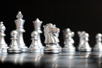 Silver knight chess piece stand in front of team on black background (Concept for leadership,...