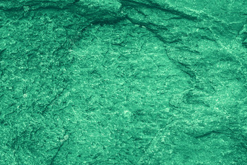 Vintage green background. Rough painted wall of emerald color. Imperfect plane of virid colored. Uneven old decorative toned backdrop of green tint. Texture of emerald hue. Ornamental stony surface.