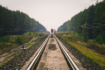 Mystic train travels by rail along forest. Railway traffic light and locomotive on railroad in distance. Mirage on railway track. Atmospheric landscape.