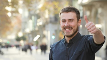 Front view of a happy man gesturing thumbs up with copy space in the street