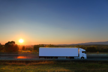 White truck transport on the road and cargo at sunset - obrazy, fototapety, plakaty