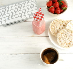 Healthy working life style banner . Laptop, notebook, cup of coffee, strawberries smoothie  and rice waffles on white wooden table. Top view, flat lay