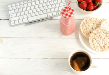 Healthy working life style banner . Laptop, notebook, cup of coffee, strawberries smoothie  and rice waffles on white wooden table. Top view, flat lay