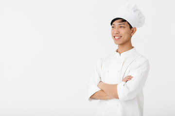 Portrait of young chinese man in white cook uniform and chef's hat smiling at camera