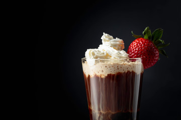 Chocolate drink with whipped cream and strawberry on a dark background.