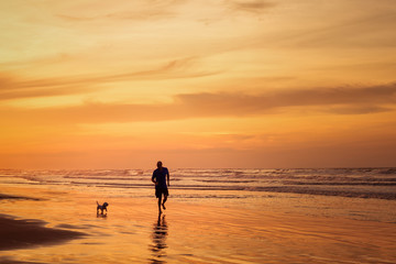 Fototapeta na wymiar Silhouette of man running with dog in the beach in sunset time