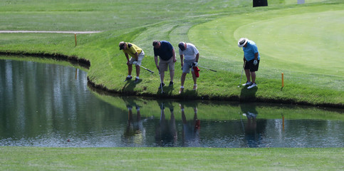 A group of golfers search for a ball that plugged into the bank of a pond