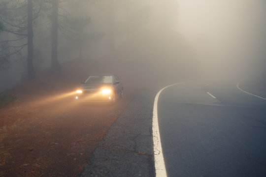 dense mist forest road and car on the roadside with light beams