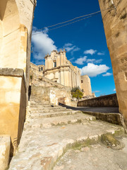 Bottom view of a pedestrian path, with the stairs that become always narrowest and that conduct to a traditional church in Matera, passing in the middle of two ancient walls