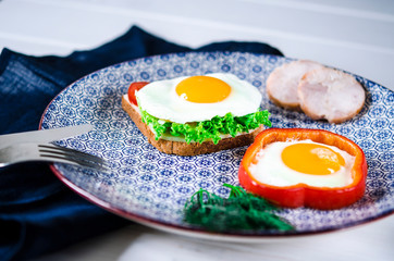 Sandwich with egg, ham, cheese, toast and salad leaves lies on a plate with tomato and dill