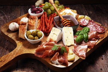 Cutting board with prosciutto, salami, cheese,bread and olives on dark wooden background