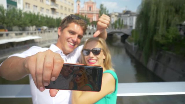 SLOW MOTION, CLOSE UP, DOF: Young couple waving at the camera while skyping from picturesque Slovenian capital city. Happy man shooting a video with his girlfriend as they explore sunny Ljubljana.