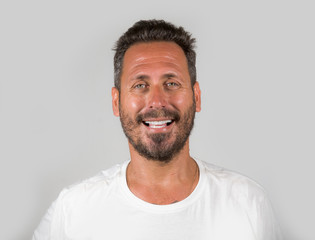 portrait of young happy and attractive man with blue eyes and beard looking cool smiling happy and confident wearing white t-shirt isolated on studio background