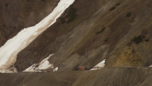 Close up low-angle still shot of a large sheet of thick Himalayan glacier flowing down ar tes, partially covering part of a mountain pass, causing causes some vehicles to stop and give way, Ladakh