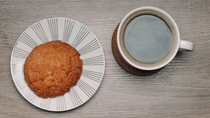 Top view - a white cup of coffee and oatmeal cookies on a saucer  on wooden background. Copy space. The concept of breakfast or snack.