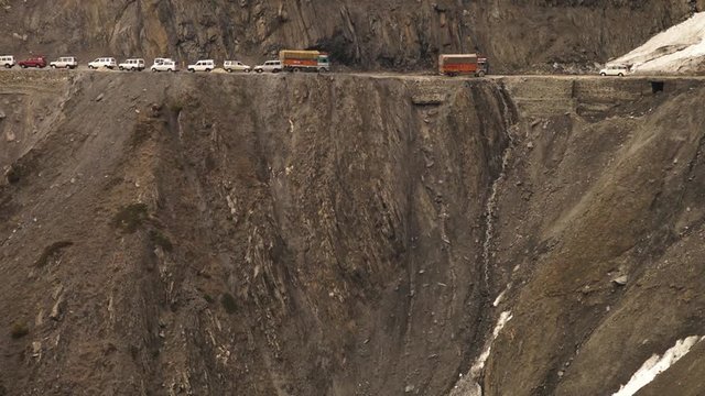 Medium high-angle still shot of off-road vehicles moving downhill, stopping to give way for those travelling uphill. Indian Himalayan glacier has blocked one side of the dangerous mountain pass