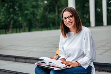 Smiling young woman sitting on stairs outdoors, reading, studying.