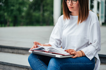 Close-up image of student girl reading while sitting on the stairs outdoors.