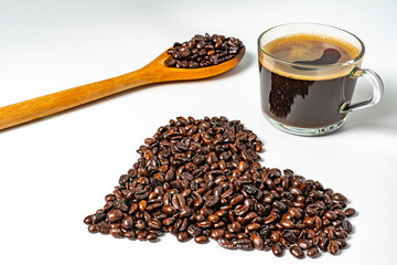 Close up black coffee in clear glass cup  with dark roasted coffee bean form in heart shape and wood spoon on white background. I love coffee concept
