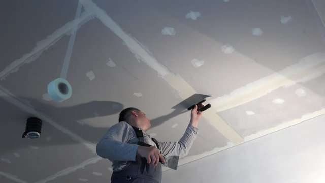 Skilled worker man spackling gypsum drywall ceiling with trowel