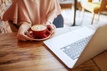 Close up of elegant Caucasian woman sitting in cafeteria and drinking espresso. In front of her on desk laptop.