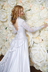 Elegant bride in a long vintage dress back view on the background of a photo zone of large white roses.