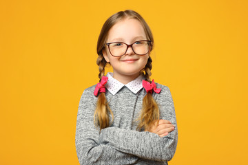 Closeup portrait of a funny little girl in glasses on a yellow background. Child schoolgirl folded...