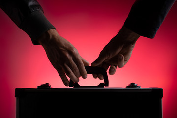 A man passes a metal case to another man. Close-up. Red background.
