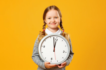 Closeup portrait little girl child holding big clock on yellow background. The concept of...