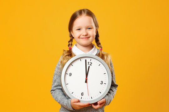 Closeup portrait little girl child holding big clock on yellow background. The concept of education, school, time management, development, timing, time to learn.