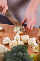 young woman in a gray aprons cuts cauliflower broccoli