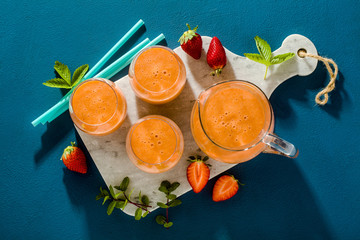 strawberry smoothies in a carafe and glasses on a blue background. raw breakfast