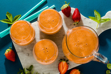 strawberry smoothies in a carafe and glasses on a blue background. raw breakfast