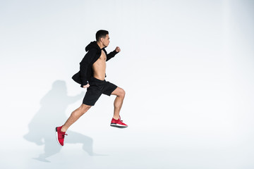 Fototapeta na wymiar side view of sportive mixed race man in black sportswear running on white