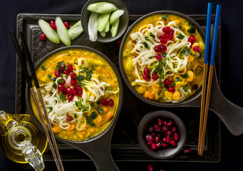 laks with pumpkin and coconut milk, rice noodles, broccoli and pomegranate seeds in portioned black plates onlaksa with pumpkin and coconut milk, rice noodles, broccoli and pomegranate seeds 
