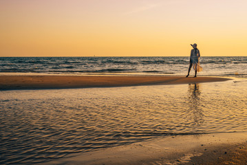 A young woman stands on the beach during a sunset, summer vacation.
