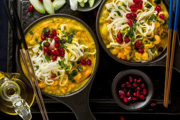 laks with pumpkin and coconut milk, rice noodles, broccoli and pomegranate seeds in portioned black plates onlaksa with pumpkin and coconut milk, rice noodles, broccoli and pomegranate seeds 