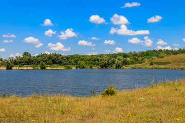 Summer landscape with beautiful lake, green meadows, hills, trees and blue sky