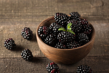 Fresh organic ripe blackberries in a wooden bowl on wooden background. Healthy rustic food concept.