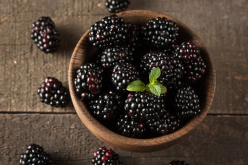 Fresh organic ripe blackberries in a wooden bowl on wooden background. Healthy rustic food concept.